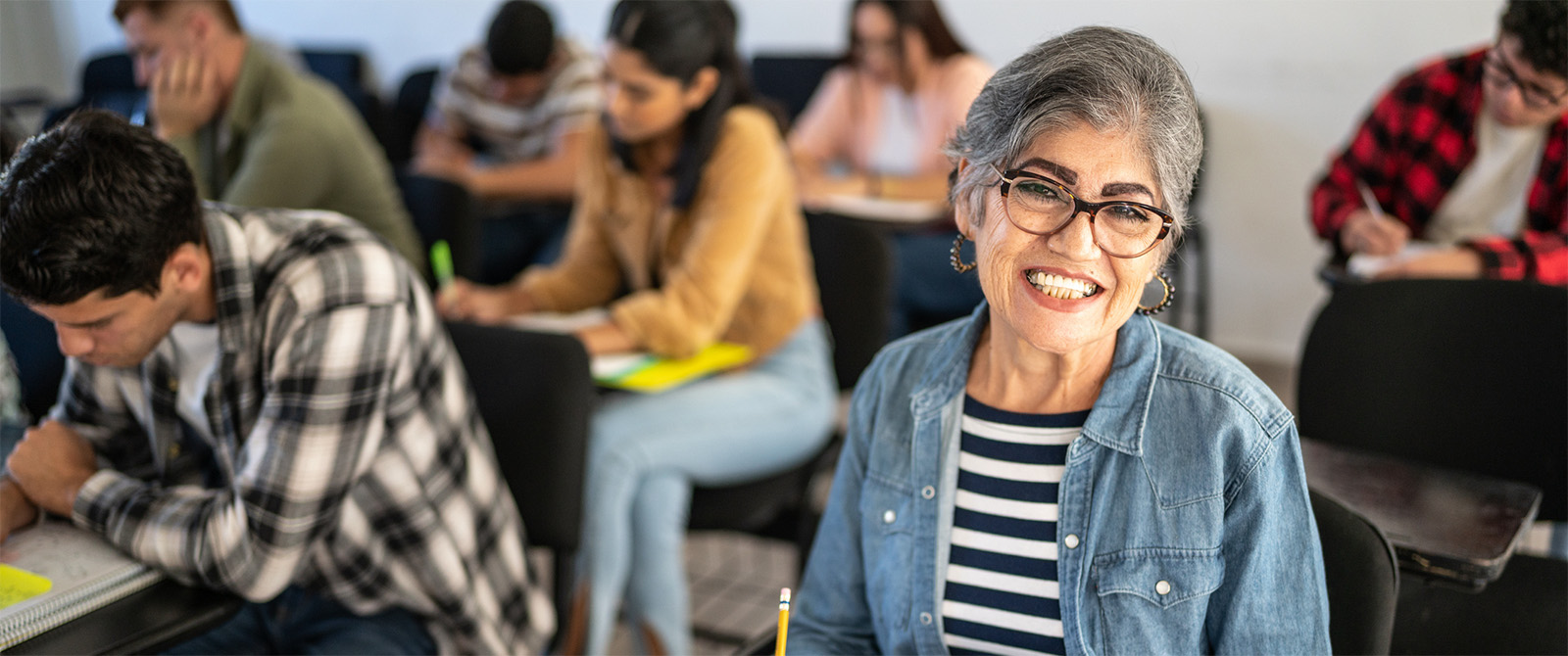 photo of senior citizen taking notes in a class full of students and smiling at camera