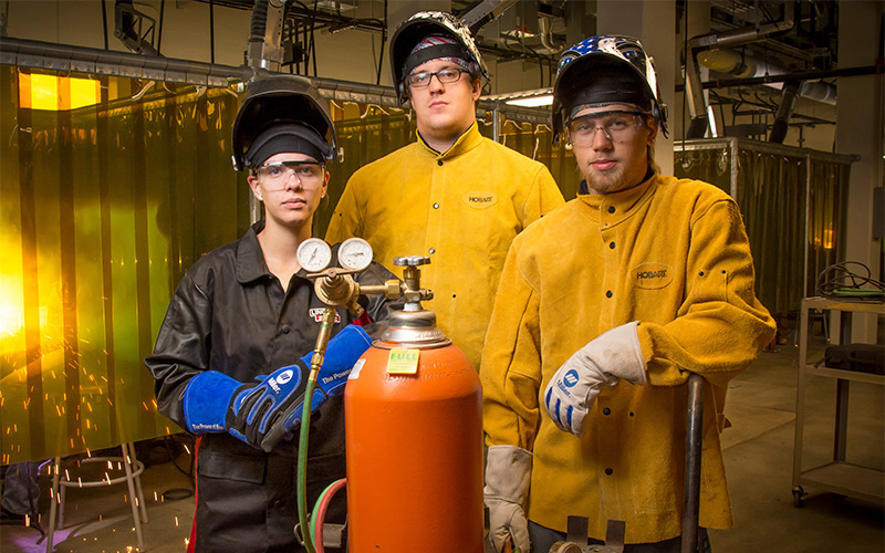 Welding students in their gear standing around equipment in a lab setting