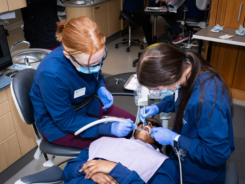 Two dental assisting students working on the teeth of a patient in a lab.