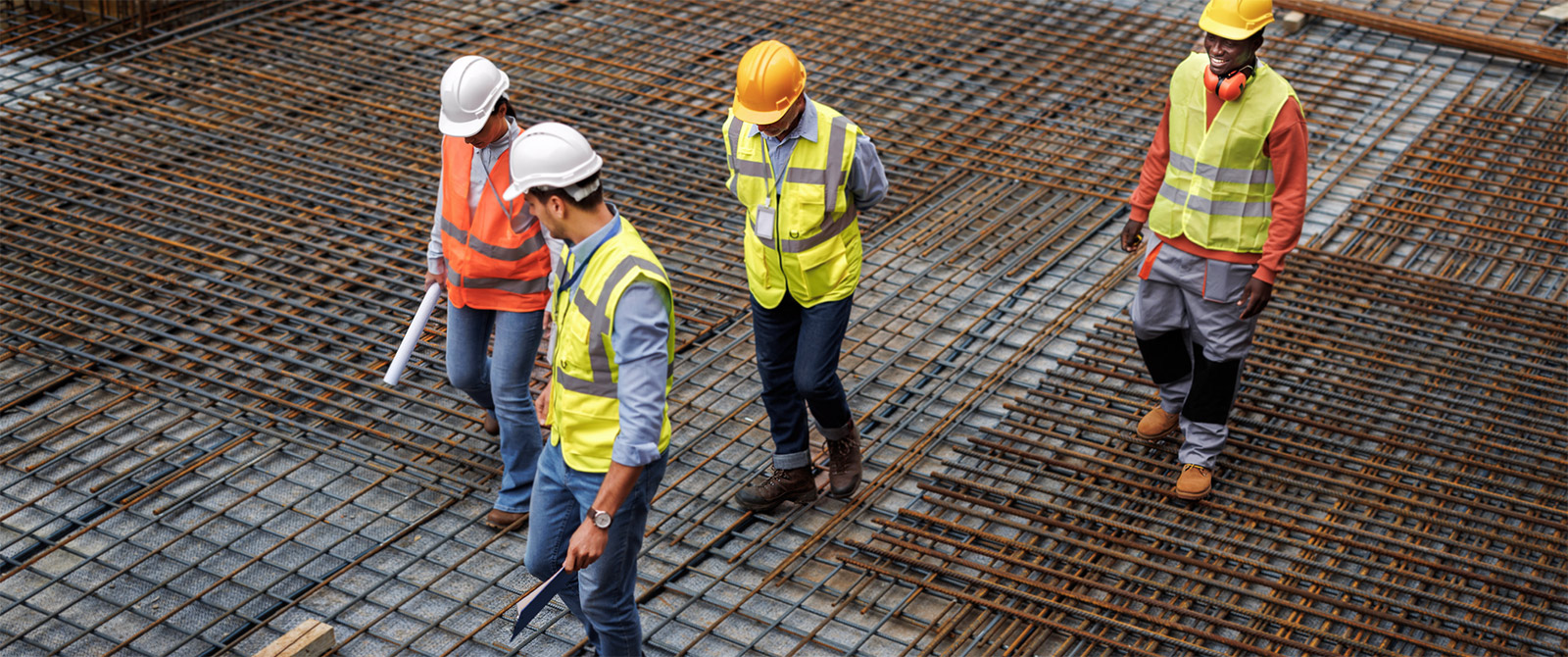 A group of workers walking carefully across an uneven surface wearing safety vests and helmets.