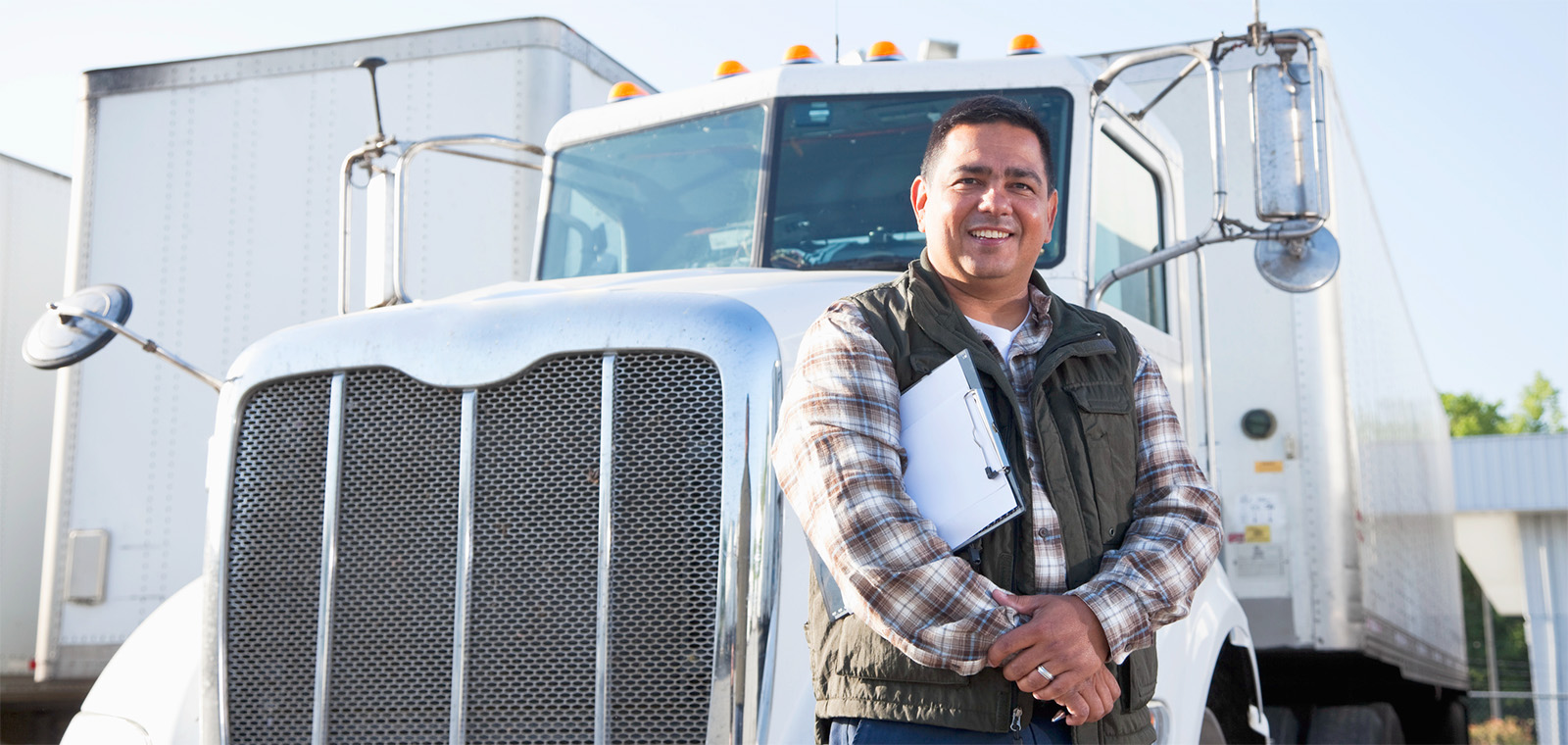 CDL Instructor standing in front of a semi-trailer holding a clipboard smiling at the camera