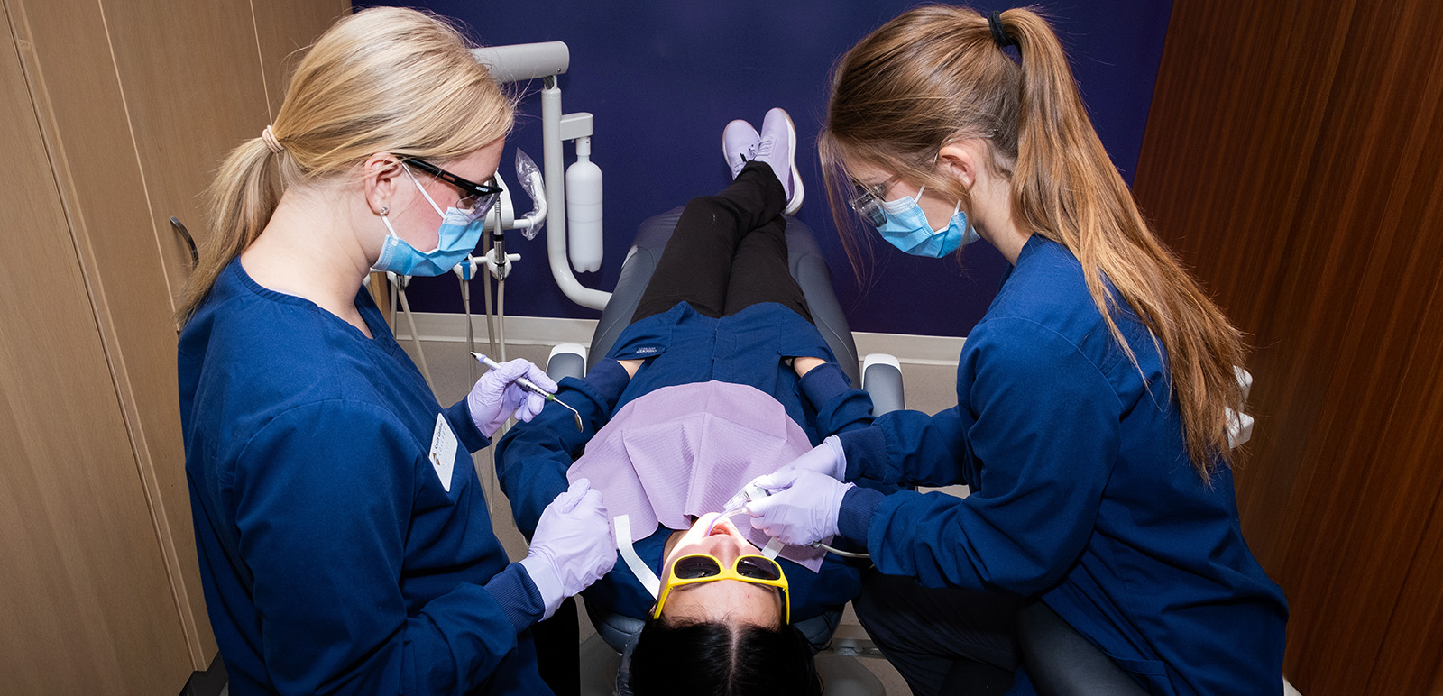 Two dental assisting students working on a patient in a dental lab.