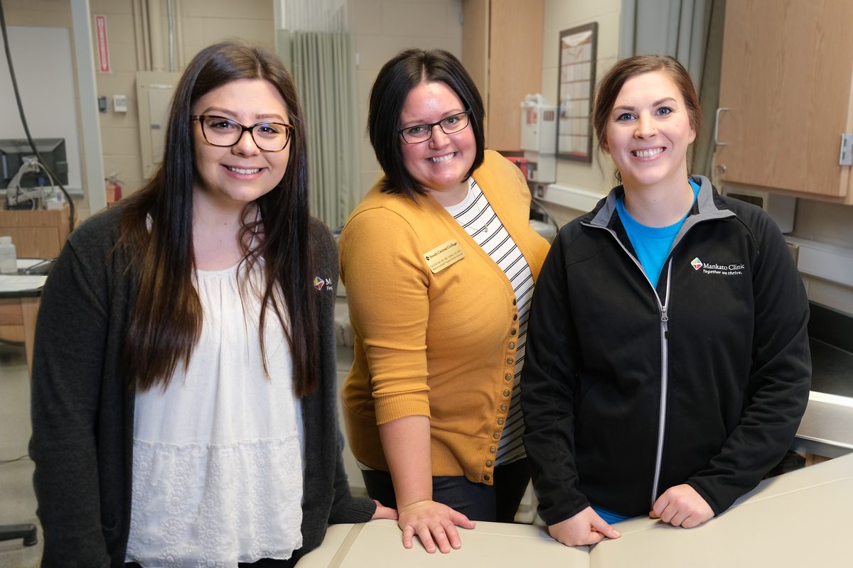 Three medical assisting program members stand together and smile in a campus lab.