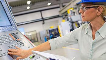 Woman in a hard hat operating a computer control panel in a manufacturing facility