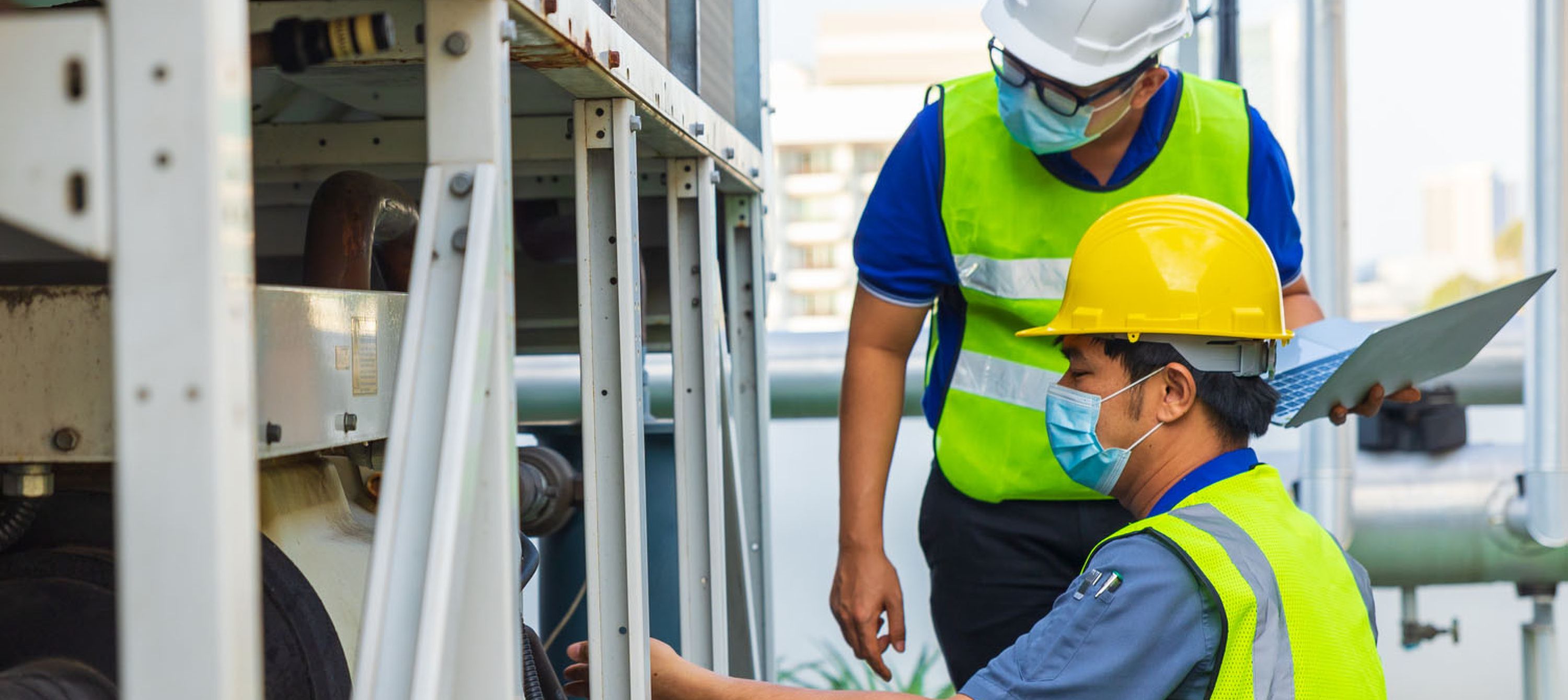 Photo of two workers wearing hard hats, safety glasses, and face masks working in industrial setting.