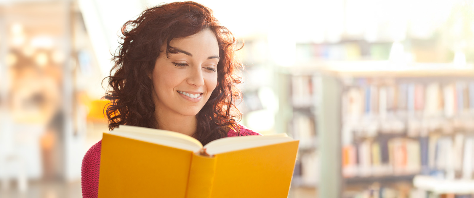 Woman smiling while reading a book in library.